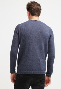 Marinblå stickad tröja med strukturerad yta, rund halsringning och ribbade muddar och nederkant, visad bakifrån mot en vit bakgrund.