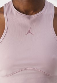 Lys rosa trenings tank top laget av glatt stoff, med en subtil logo i midten og buede sømdetaljer nær kanten.