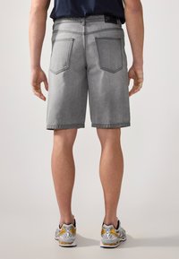 Gray denim shorts with a straight cut, visible stitching, and two back pockets, paired with gray and yellow athletic shoes.