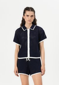 Set a due pezzi in maglia blu navy, composto da un top a maniche corte con rifiniture bianche e chiusura a bottoni, abbinato a pantaloni corti coordinati, entrambi con una texture in rete.
