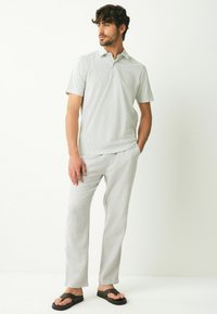 Lys grå mønstrede polo skjorte med korte ærmer, parret med lys grå afslappede bukser og sorte klipklappere. Causal outfit.