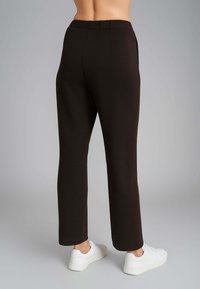 Pantaloni neri su misura con un design a gamba dritta e una texture liscia. Presentano una vita e tasche, abbinati a sneaker bianche.