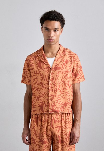Ein kurzärmliges Hemd und passende Shorts in Korallen- und Orangetönen, die ein sich wiederholendes Blättermuster und ein lässiges Knopfdesign aufweisen.