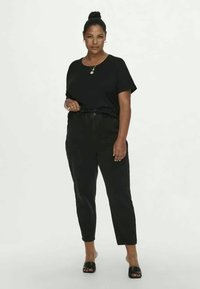 Top preto de mangas curtas combinado com calças pretas de cintura alta, apresentando um corte relaxado e textura suave; modelo usa chinelos pretos.