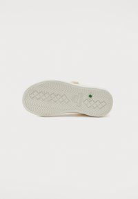 Valge sneakersoole lainemuster, kummimaterjal ja roheline aktsent kanna lähedal. Omab embosseeritud logo detaili.