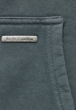 Dark gray fabric with a textured finish, featuring a metal label that reads "bazix republiq" sewn onto the surface.