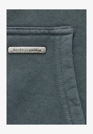 Dark gray fabric with a textured finish, featuring a metal label that reads "bazix republiq" sewn onto the surface.