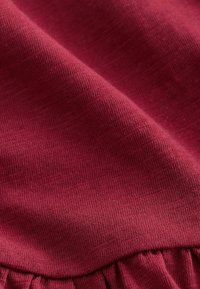 Textile bourgogne avec une finition douce et texturée ; présente un ourlet inférieur froncé ajoutant du détail à l'ensemble du design.