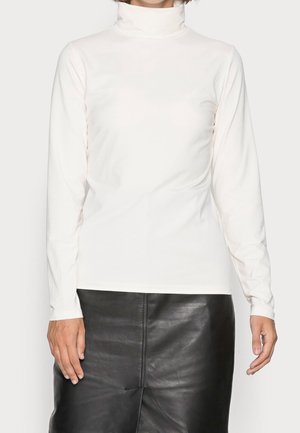 Person wearing a white long-sleeve turtleneck top paired with a black leather skirt, hands relaxed at sides.
