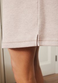 Gebreide lichtroze jurk met een gestructureerd patroon, gespleten zoom en gestikte details langs de onderrand.