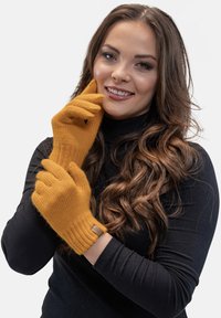 Pletené rukavice v hořčičně žluté barvě mají ribbed strukturu, přiléhavý design a malý štítek na manžetě pro identifikaci značky.