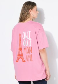 Rosa übergroßes T-Shirt mit einem Grafikdruck des Eiffelturms und dem Text "Oui Oui Mon Ami" in Weiß und Orange. Weiches Baumwollmaterial.