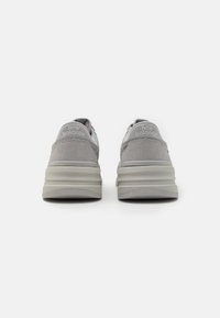 Sive teniske s tenisicama od antilopa i mrežastih materijala, s debelim potplatom, ojačanim petom i utisnutim "New Balance" logotipom na stražnjoj strani.