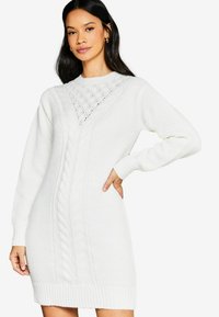 Rochie tricotată albă, cu un design din tricot înfășurat, manșete și tivuri cu nervuri, cu un model texturat la guler și o croială lejeră.