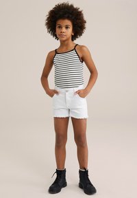 Gestreept zwart-wit tanktop gecombineerd met rafelige witte denimbroekjes. Zwarte veterschoenen maken de outfit af en benadrukken een casual uitstraling.