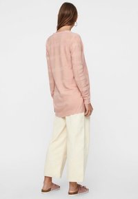 Różowy, jasny sweter z długim rękawem w teksturowane paski, zestawiony z kremowymi spodniami o szerokich nogawkach oraz różowymi sandałami wsuwanymi.