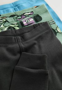 Trois paires de leggings en coton : en haut en bleu clair, au milieu en vert avec un motif cartoon, en bas en gris foncé avec des poignets côtelés.