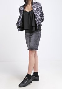 Top negro sin mangas colocado debajo de una chaqueta bomber de estampado de leopardo gris, combinado con una falda de mezclilla descolorida y zapatillas negras con acentos en contraste.