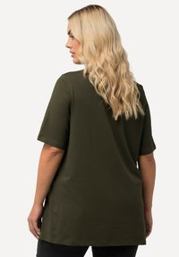 Diepgroene t-shirt met korte mouwen, gemaakt van zachte stof. Heeft een ontspannen pasvorm en een iets langere achterkant, met een gladde textuur.