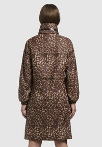 Hnedo-bežový kabát s leopardím vzorom a vysokým golierom, dlhými rukávmi a elastickými manžetami; má zúžený pás a zadnú vrecko.