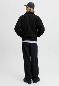 Zwarte sweatshirt met een hoge kraag, gecombineerd met grijze lagen eronder en donkere broek. Soepele textuur, relaxte pasvorm, minimale merkdetails.