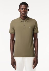 Rövid ujjú olajzöld pólóing, textúrált anyagból készült, gallérral, három gombos gombolással és egy kisebb Lacoste logóval a mellkasán.