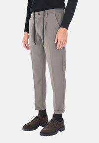 Pantaloni grigi chiari su misura con pieghe, vita con cordoncino e risvolti, abbinati a scarpe in suede marrone scuro e calze nere.