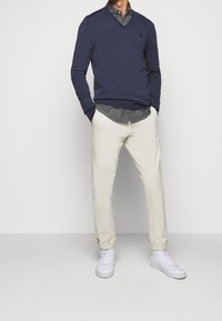 Suéter de punto en navy con escote en v, camisa de botones gris, chinos color crema y zapatillas blancas. Ajuste relajado, material de algodón y puños de pantalón doblados.