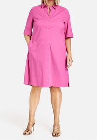 Robe boutonnée rose à manches courtes, en tissu lisse. Comprend des poches latérales et une coupe évasée jusqu'aux genoux.