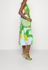 UDSKÆRETS BLOMSTERKJOLE I LYSEBLÅ MED GUL BANAN OG GRØNNE BLADMØNSTRE, SAMMENPAIRING MED EN GRØN VEVET TASKKE OG STRAPPEDE GRØNNE HØJE HÆLE.