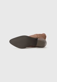 Brown suede ankle boot with tapered toe, low heel, and textured rubber sole. Interior has a zip closure for easy wear.