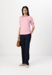 Stripet langermet topp i rosa og hvit, med en liten logo. Kombinert med marineblå vide bukser og beige leiligheter. Brun skulderveske.