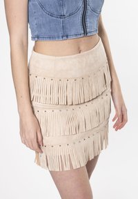 Beige suède mini-rok met gelaagde franjes, zilveren studaccenten en een soepele textuur, gecombineerd met een blauwe denim cropped top.