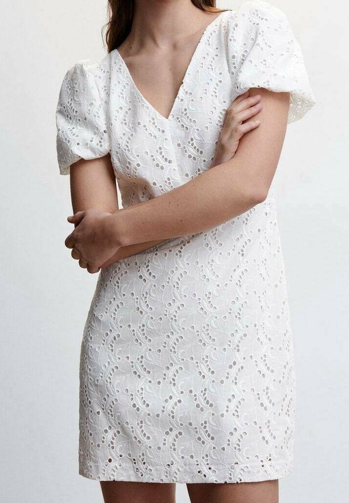 Robe courte blanche avec manches bouffantes, col en V et motifs en dentelle découpée complexes. Le tissu semble texturé et léger.