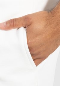 Weißer Stoffbeutel mit teilweise eingeführter Hand. Glatte Textur, die feine Stitching-Details rund um die Öffnung des Beutels zeigt.