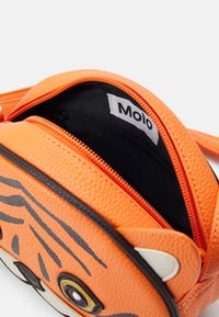 Oranssi keinonahkainen laukku, jossa on tiikerin kasvokuvio, ylhäällä vetoketju, musta sisävuori ja pieni sisätasku, jossa on etiketti.