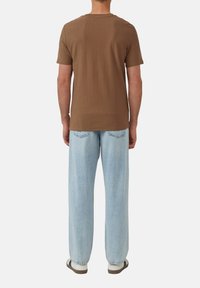 Braunes, strukturiertes T-Shirt mit kurzen Ärmeln, getragen zu hellblauen, lockeren Jeans mit geradem Schnitt und Taschen.