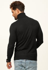 Black, knitted sweater with a high collar and long sleeves. Smooth texture and ribbed hem detail. Paired with light blue jeans.
