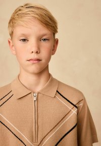 Beige lühikeste varrukatega polo särk, millel on tõmblukk kaeluses, musta ja valge diagonaalse triibuga. Pehme kangas, millel on sile tekstuur.