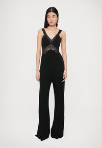 Salopetă neagră cu dantelă la corset, bretele reglabile și design cu picioare largi pentru o siluetă fluidă.