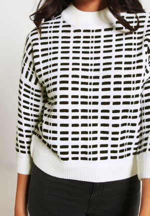Pull blanc avec un motif en quadrillage noir, col et poignets côtelés, tissu texturé et coupe décontractée.