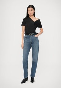 Juodas aptemptas viršus su atvirais pečiais ir gėlių detalėmis, derinamas su aukštu liemeniu mėlynais džinsais ir juodais aulinukais aukštu kulnu.