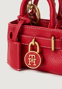 Punane tekstuuriga nahast käekott, millel on valged õmblused, kullast metallist rõngas käepidemetega ning ümmargune kullast ja punane lukukäepide, millel on reljeefi tähed.