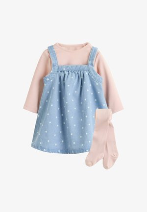 Camiseta rosa de manga larga con canalé con medias a juego debajo de un vestido tipo peto de mezclilla azul claro con lunares blancos para un niño pequeño.