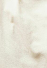 Fond en tissu beige clair avec une texture subtile et de doux plis, créant des ombres et des reflets délicats.