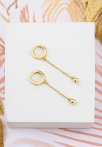 Guld hoop øreringe har hængende kæder med runde, polerede vedhæng. Designet er minimalistisk og elegant, hvilket forstærker deres glans.