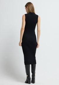 Czarna dzianinowa sukienka o dopasowanym kroju, bez rękawów, długości midi, zestawiona z wysokimi, czarnymi kozakami do kolan z złotym akcentem.