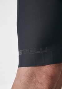 Schwarze Radsportshorts mit glatter Textur, die am Saum ein kontrastierendes dunkelgraues Logo aufweisen und eine körpernahe Passform für optimale Leistung bieten.