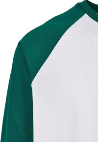 Raglan-T-Shirt mit grünen Ärmeln und weißem Körper, aus Baumwolle mit einer glatten Textur und Kontrastnähten entlang des Halsauschnitts.