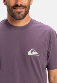 Purple cotton t-shirt featuring a white logo on the left chest area, with a classic crew neckline and short sleeves.